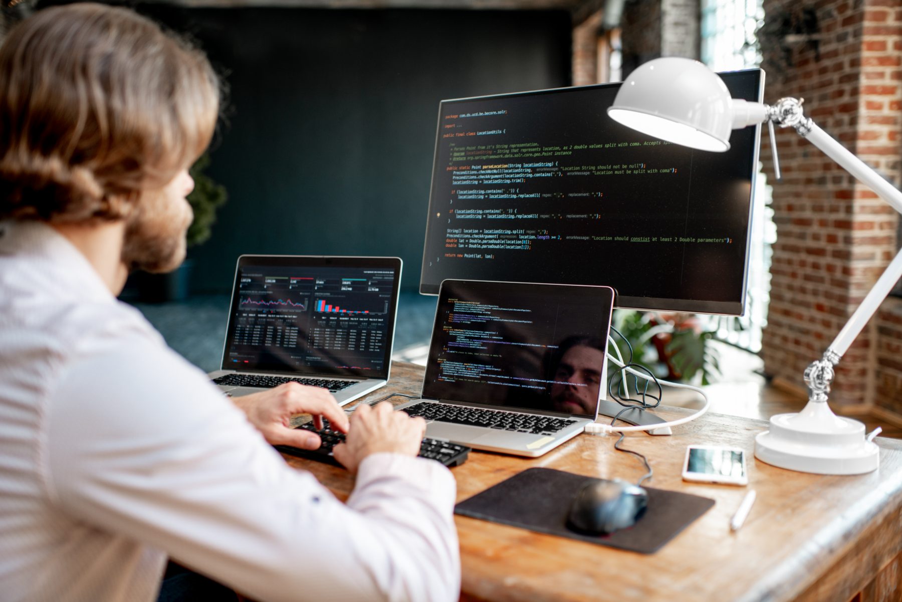 Software developer working with code and a dashboard across multiple screens