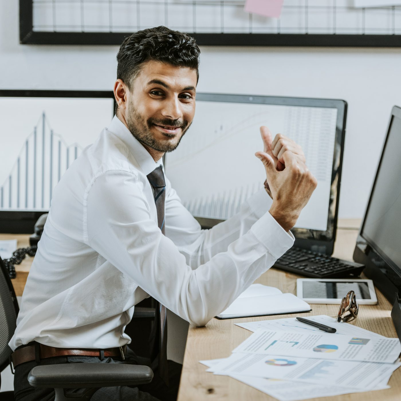 Smiling employee at a desk with charts on multiple monitors